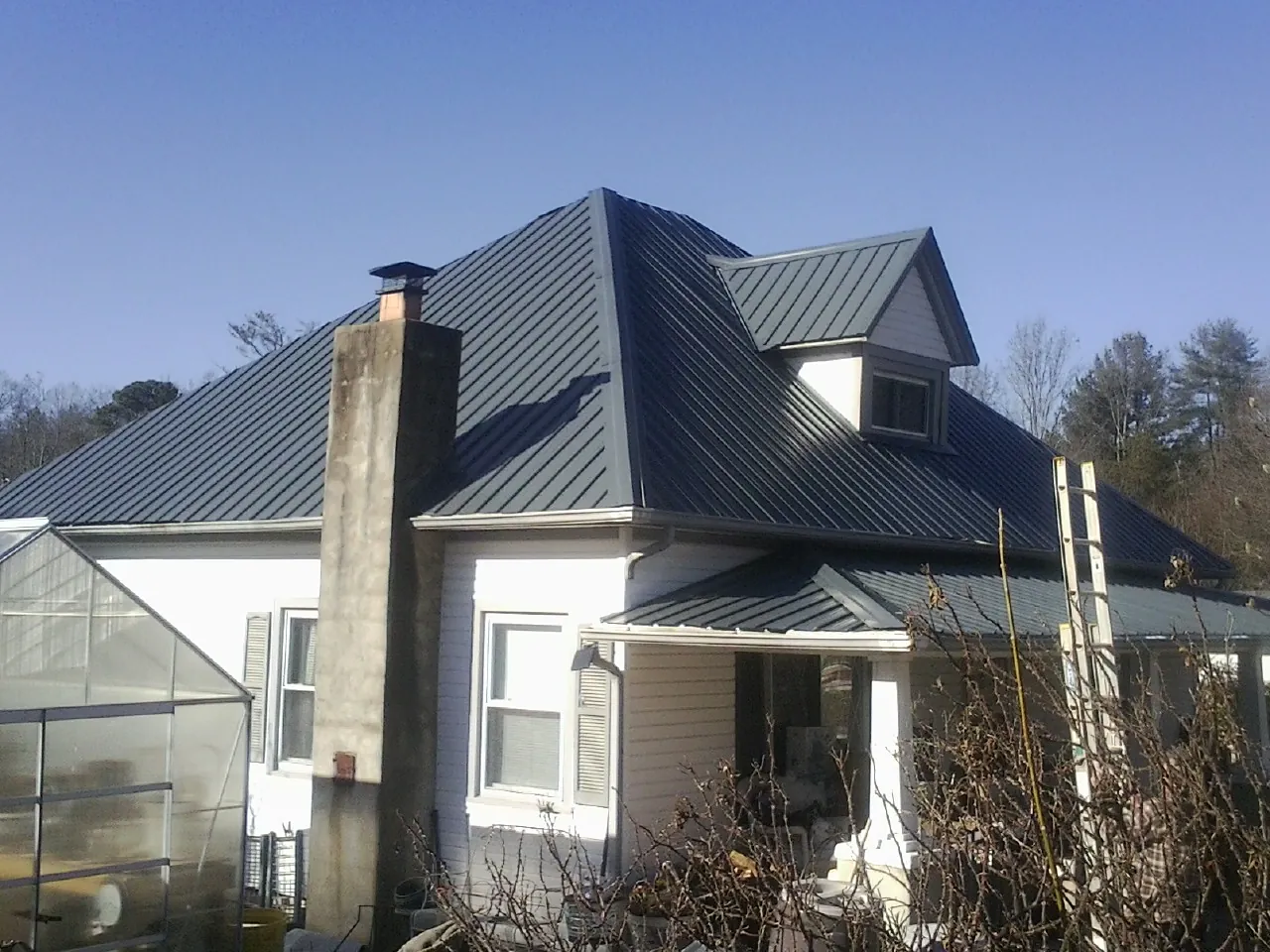 Dark blue standing seam metal roof on a white farmhouse with dormer — Slate & Tile Roof Repair by Roofing Brothers in Smiley