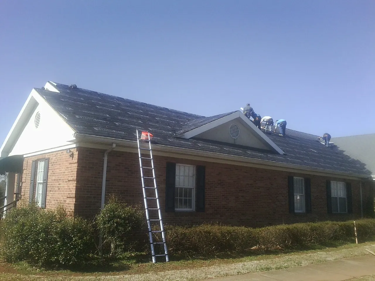 Crew tearing shingles off a brick ranch roof with a ladder set — Emergency Roof Repair work by our crew in Smiley