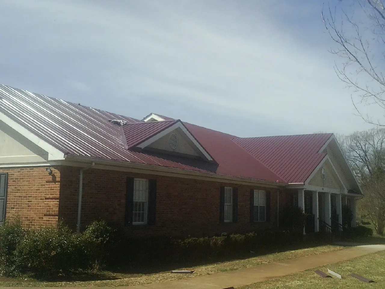 Red metal roof with gabled entries on a long brick building, from a Hail Damage Roof Repair job in Smiley